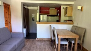 Ein kompakter Wohnbereich mit Sofa, Esstisch und Stühlen. Im Hintergrund ist eine Küchenzeile zu sehen.