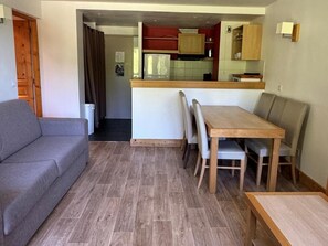 A compact living space with a sofa, dining table, and chairs. A kitchen area is visible in the background. - Ski-in/ski-out & foot of the slopes, 4th floor, view ski slopes, swimming pool, balcony, tv (La Plagne)