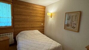 A bedroom with a wooden headboard, a bed with a white quilt, a wall-mounted light, and a framed picture. - Ski-in/ski-out & foot of the slopes, 4th floor, view ski slopes, swimming pool, balcony, tv (La Plagne)