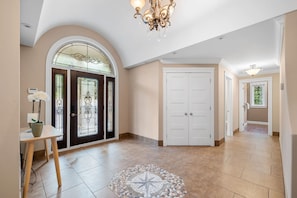 Um hall espaçoso com piso de azulejos, um tapete decorativo, um candelabro e uma porta com painéis de vidro.