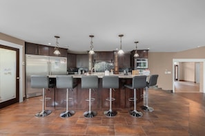 Uma cozinha moderna com uma ilha central, banquetas, eletrodomésticos de aço inoxidável e iluminação pendente.