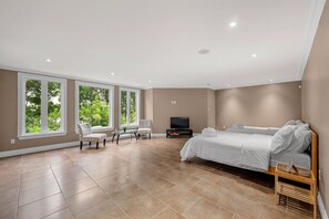Um quarto espaçoso com uma cama grande, uma televisão e um espaço de estar com cadeiras.