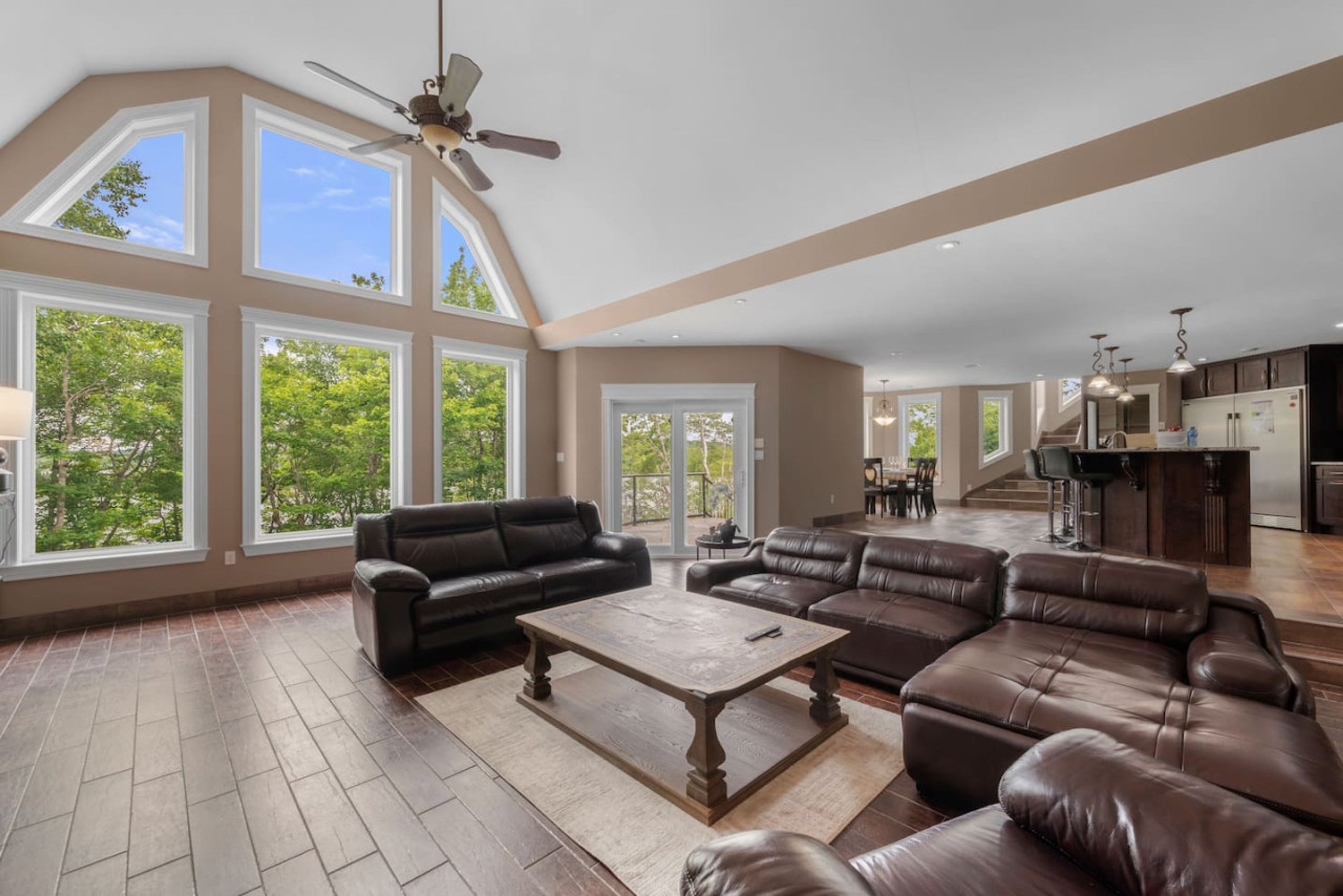 A spacious living room with leather sofas, a coffee table, and large windows offering a view of trees.