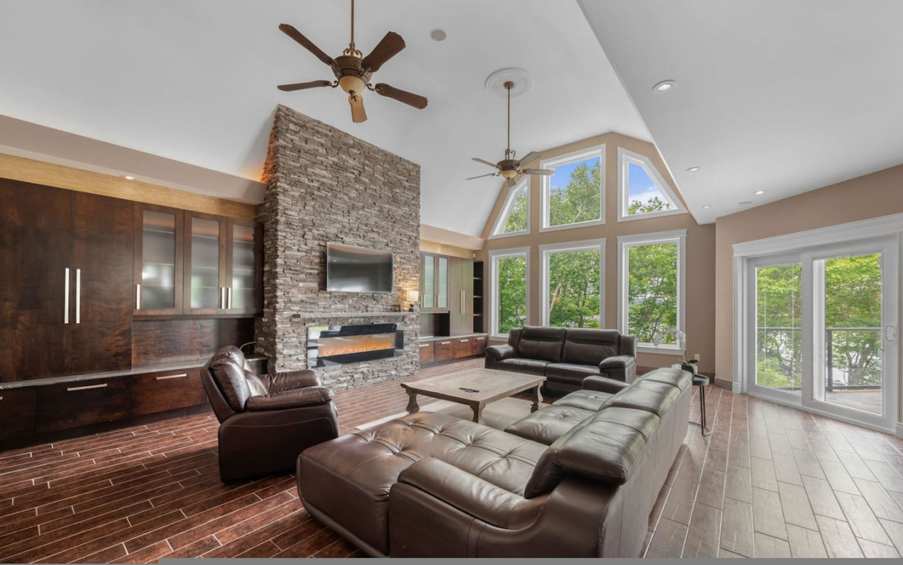 A spacious living area with a stone fireplace, leather sofas, and large windows offering a view of the outdoors.