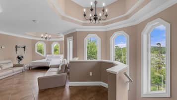 A spacious living room with a large window, a chandelier, and a modern sofa.
