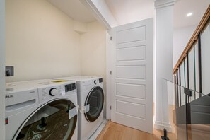 Uma lavanderia com duas máquinas de lavar LG, uma porta branca e uma escada com guarda-corpo de vidro.