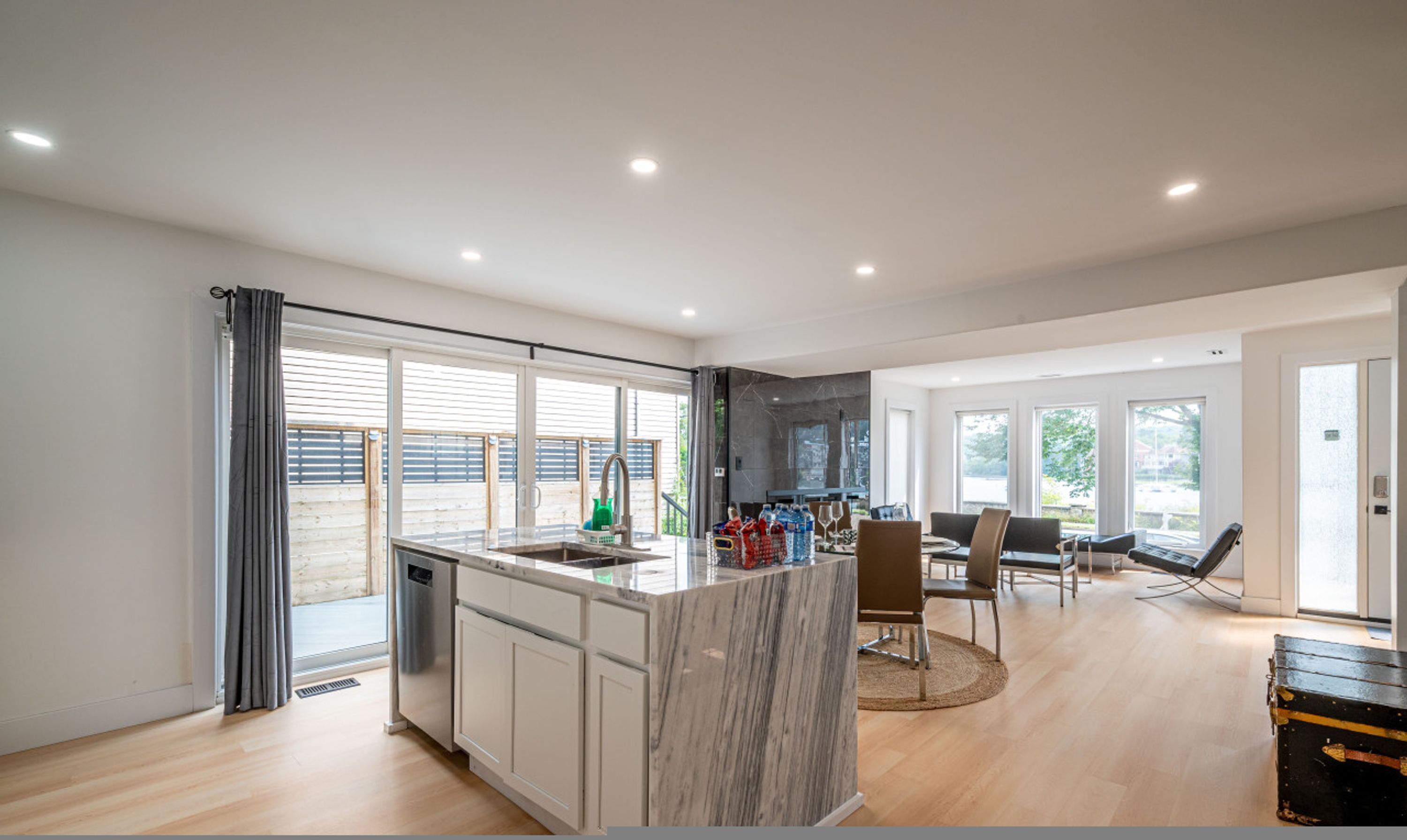 A modern kitchen with a marble island, large windows, and a dining area with chairs.