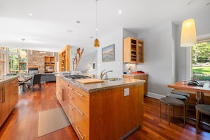 A modern kitchen with wooden cabinets, a central island, and a dining area with bar stools. - Serene Modern Lakehouse on Golf Course (Hammonds Plains)
