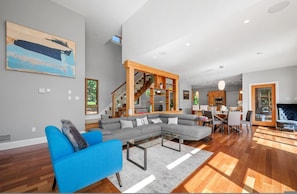 A modern living room with a sectional sofa, a glass coffee table, and a staircase leading to an upper level. - Serene Modern Lakehouse on Golf Course (Hammonds Plains)