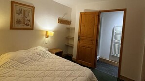 A bedroom with a large bed, a bedside table, a nightstand, a wooden wardrobe, a wall-mounted shelf, and a door leading to another room. - Ski-in/ski-out & foot of the slopes, 7th floor, view ski slopes, swimming pool, balcony, tv (La Plagne)