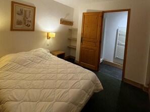 Ein Schlafzimmer mit einem großen Bett, einem Nachttisch, einem Schrank aus Holz, einem an der Wand befestigten Regal und einer Tür zu einem anderen Raum.