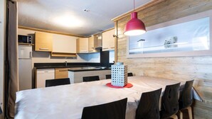 A compact kitchen with wooden cabinets, a microwave, and a stove. There is a dining table with chairs and a red pendant light.