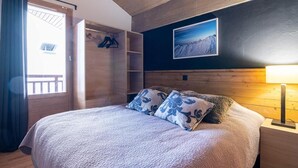 A bedroom with a bed, a wooden wardrobe, a nightstand, a lamp, and a framed picture on the wall.