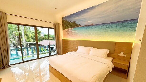 Habitación de hotel con una cama grande, vista a una playa a través de una puerta corrediza de vidrio y un cuadro de una escena costera en la pared.