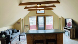 A cozy living room with a sofa, a coffee table, a wooden TV stand, and a small kitchen area with a bar counter. - Cozy loft in Gardiner with AC, WiFi and splendid views  (Gardiner)