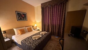 Ein Hotelzimmer mit einem großen Bett, zwei Nachttischen, einem Fernseher und einem gemusterten Teppich.
