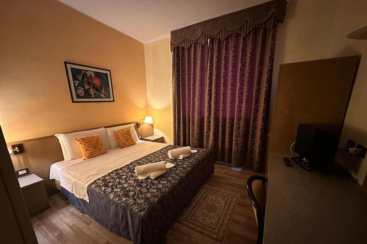 A hotel room with a large bed, two bedside tables, a TV, and a patterned rug.