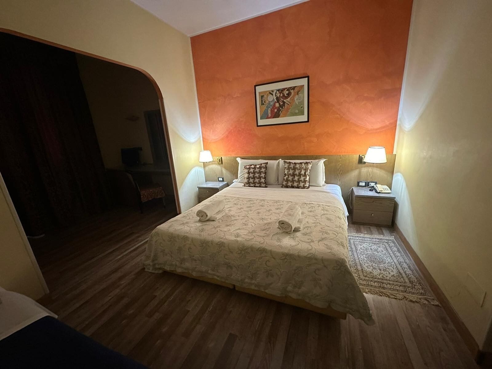 Une chambre d’hôtel avec un grand lit, deux tables de chevet avec des lampes, un tableau au mur et un plancher en bois.