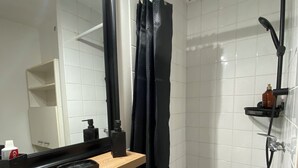 Een badkamer met een wit wastafelmeubel, een spiegel, een douchecabine en een plank met toiletartikelen.