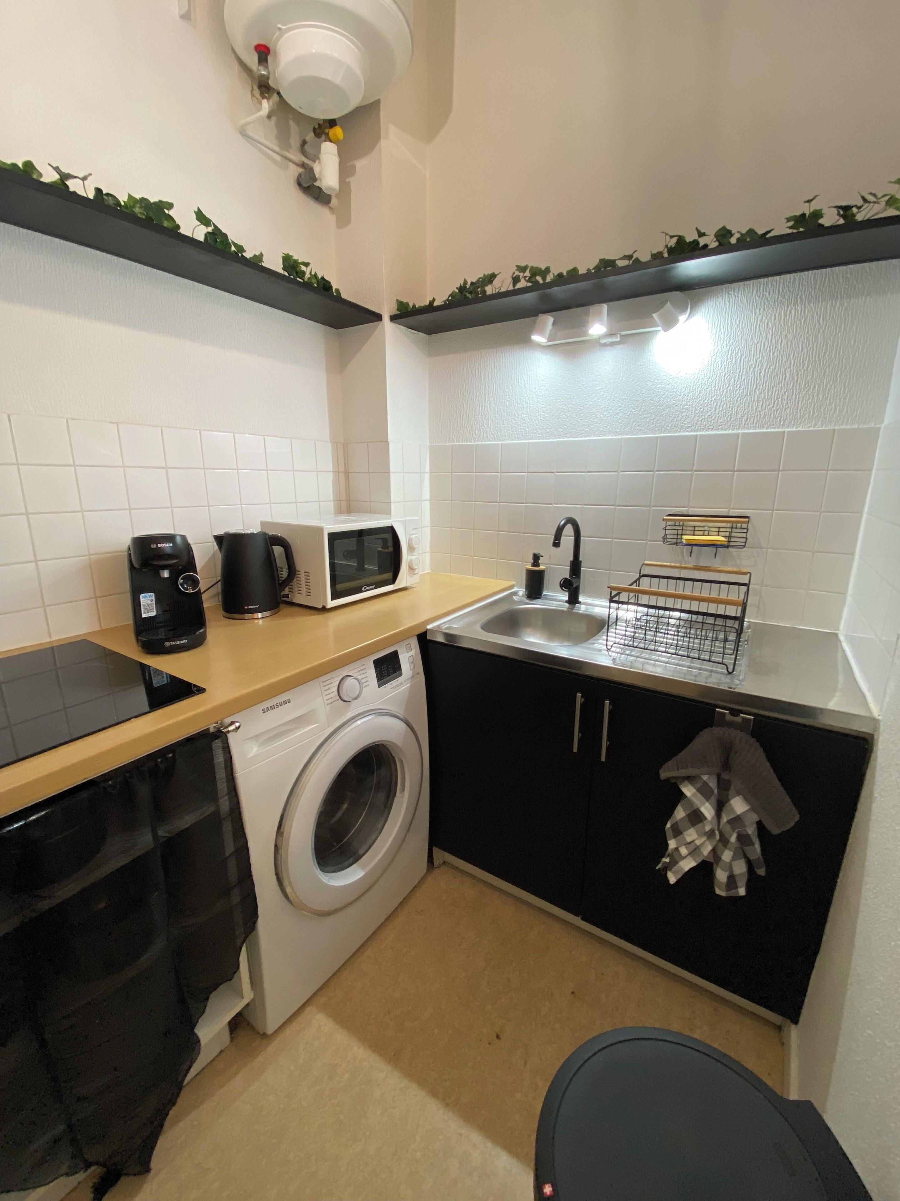 A compact kitchen with a washing machine, microwave, sink, and a small countertop.