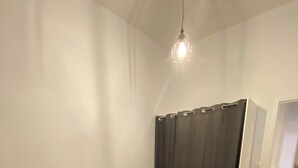 Een enkel bed met een grijze matras en kussens, een nachtkastje met een lamp, een donker gordijn en een houten vloer.