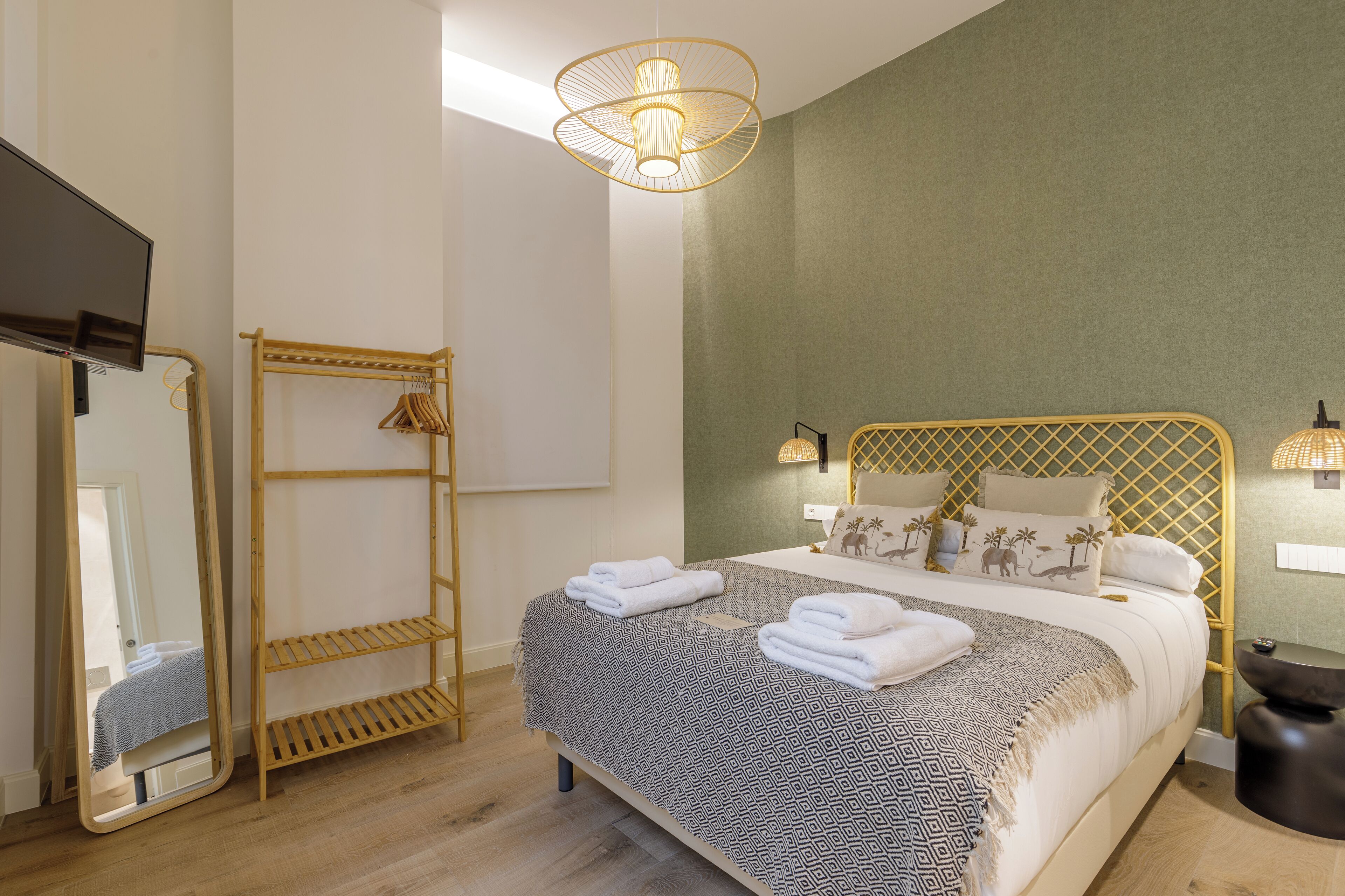 Een keurig opgemaakt slaapkamer met een bed, een houten wandplank, een spiegel en een hanglamp.