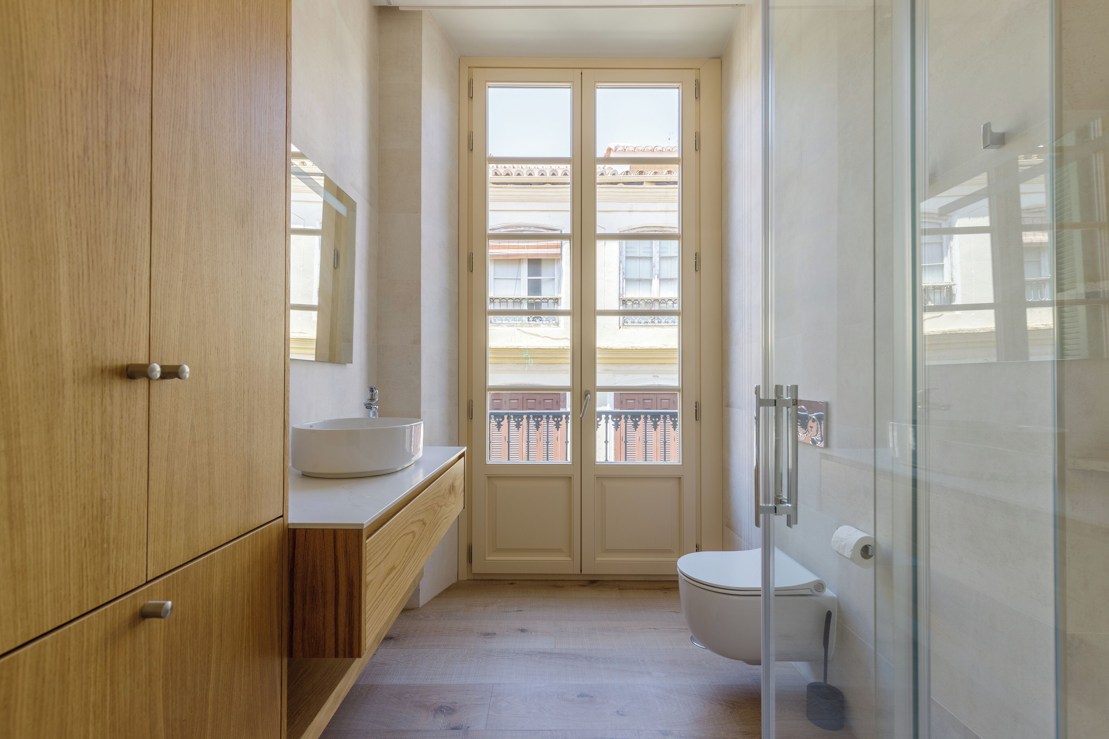 Ein Badezimmer mit Holzschrank, Waschbecken, Toilette und einer Duschkabine aus Glas.