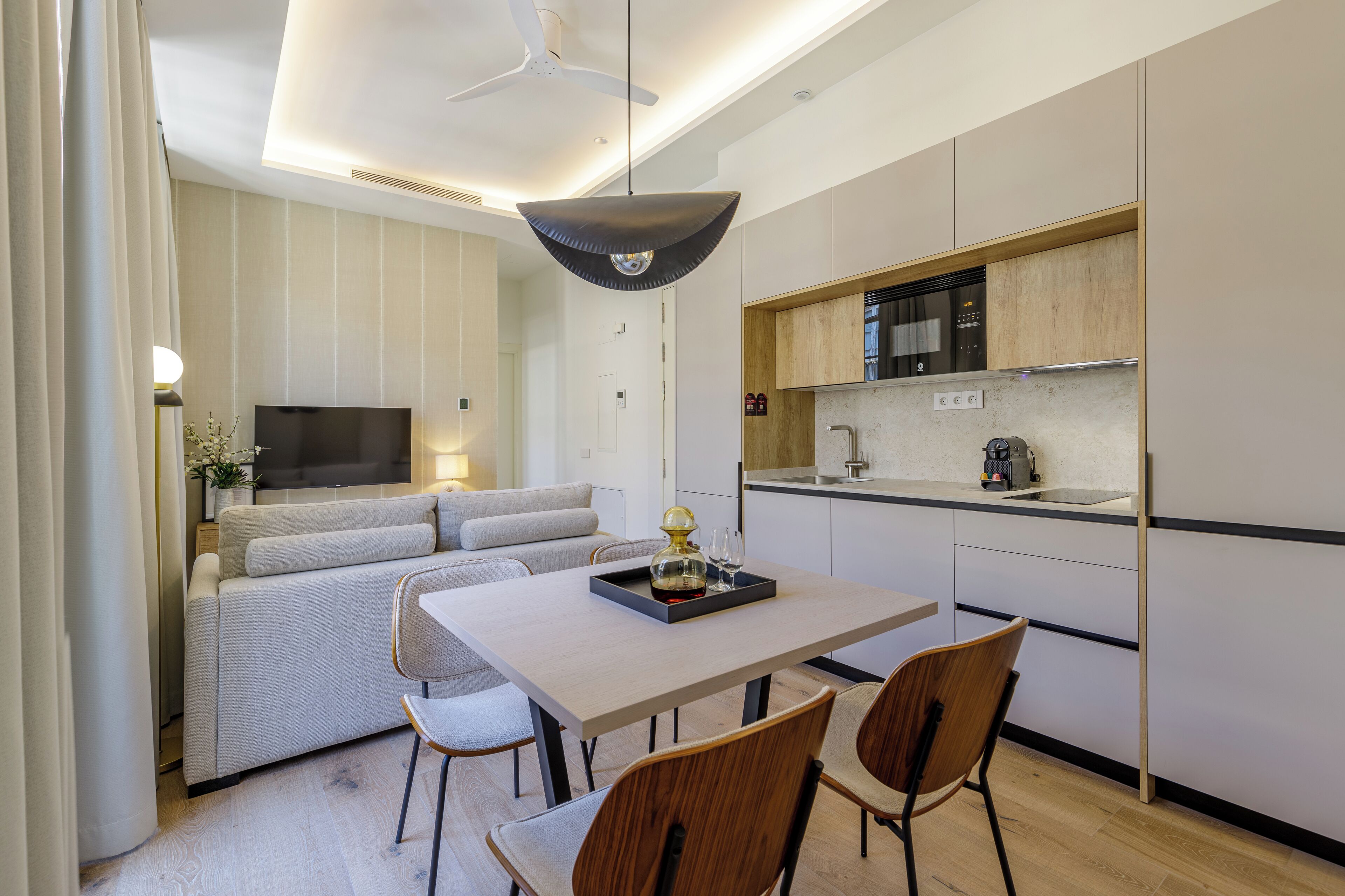 A modern living room with a sofa, a dining table with chairs, a TV, and a kitchen area with a microwave and sink.