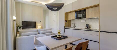 A modern living room with a sofa, a dining table with chairs, a TV, and a kitchen area with a microwave and sink.