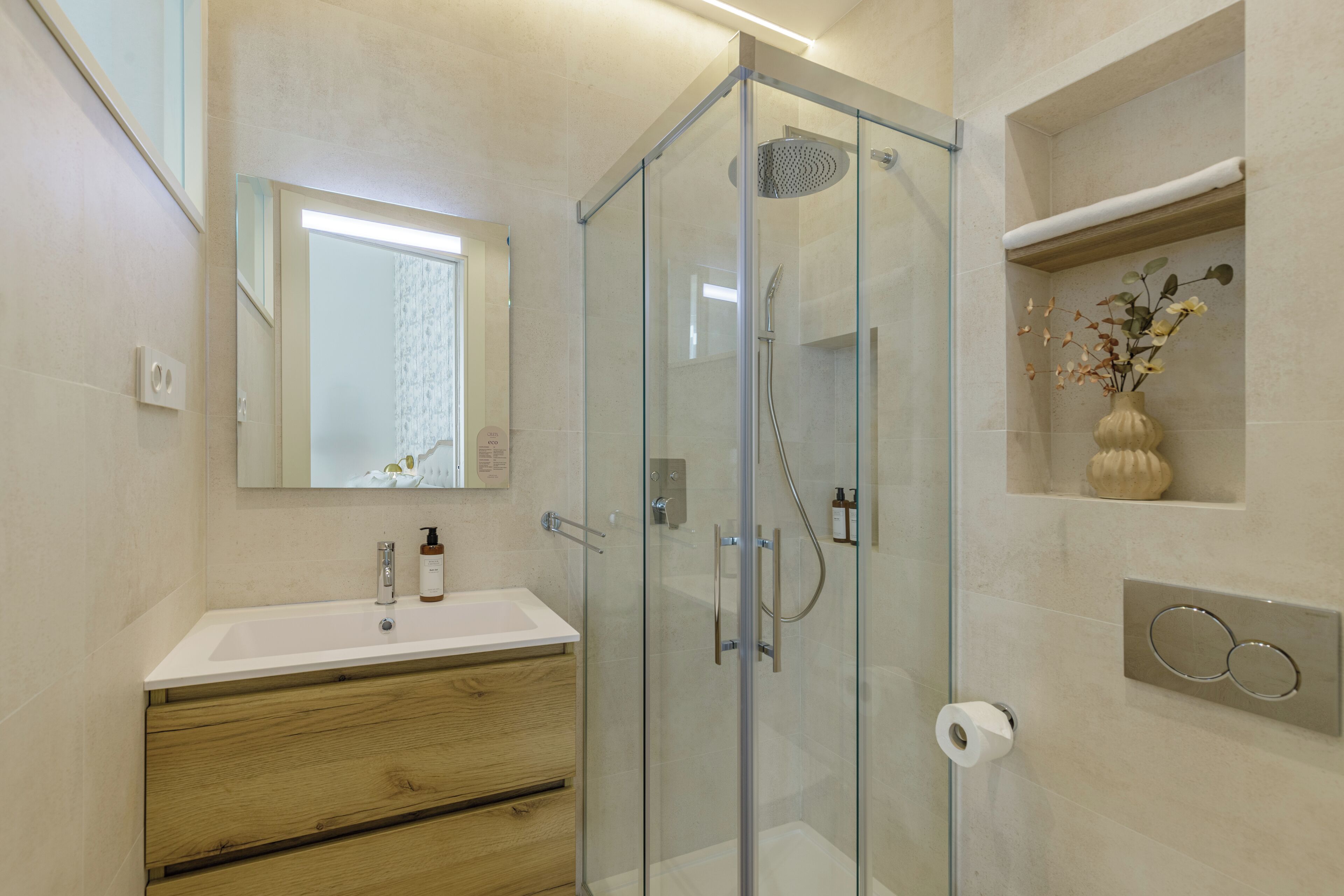A modern bathroom with a glass-enclosed shower, a white sink, wooden vanity, and a mirror.
