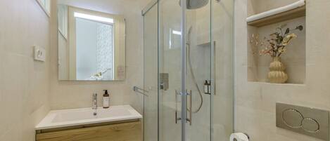 A modern bathroom with a glass-enclosed shower, a white sink, wooden vanity, and a mirror.