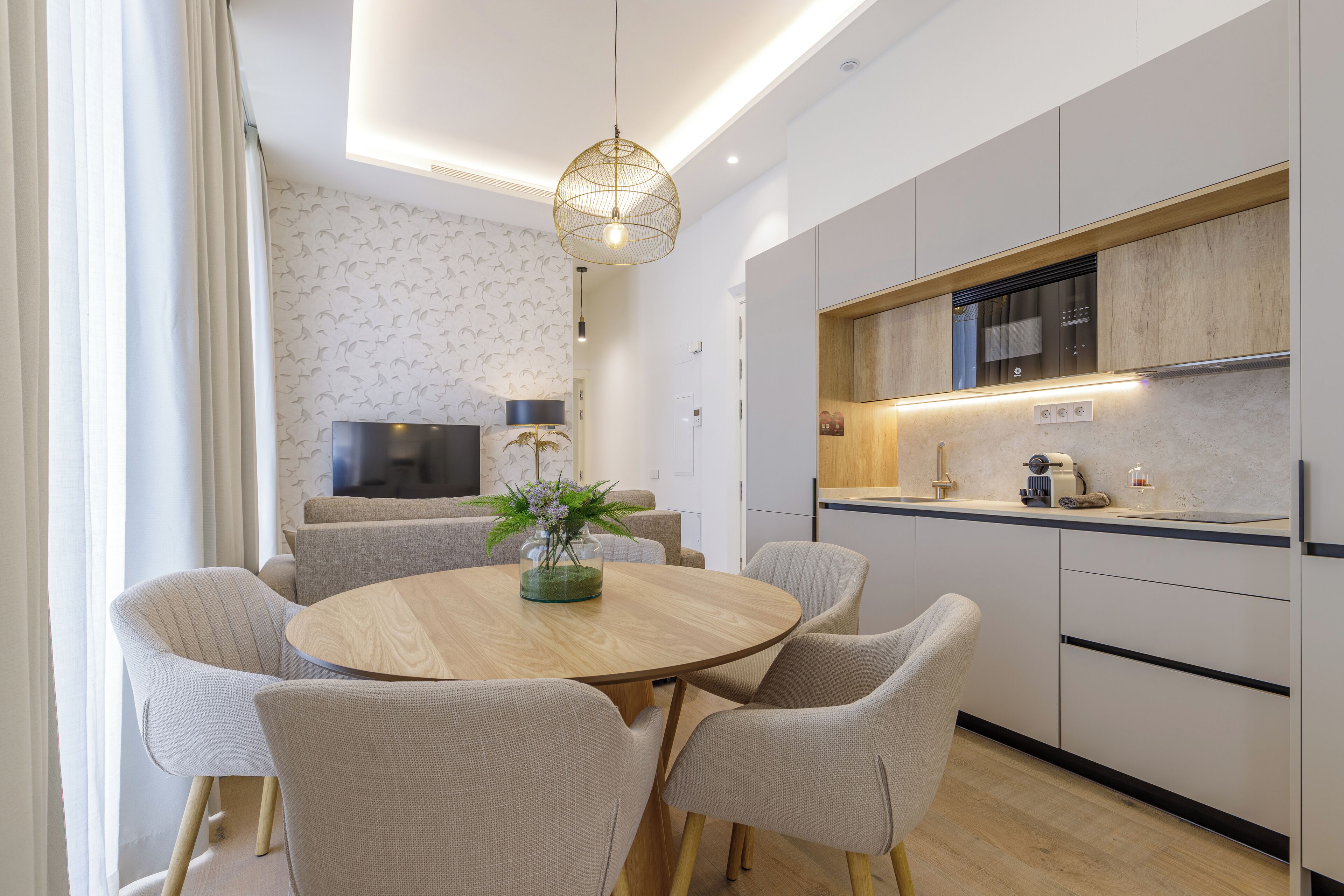 A modern kitchen with a round wooden table, six chairs, and a hanging light fixture.