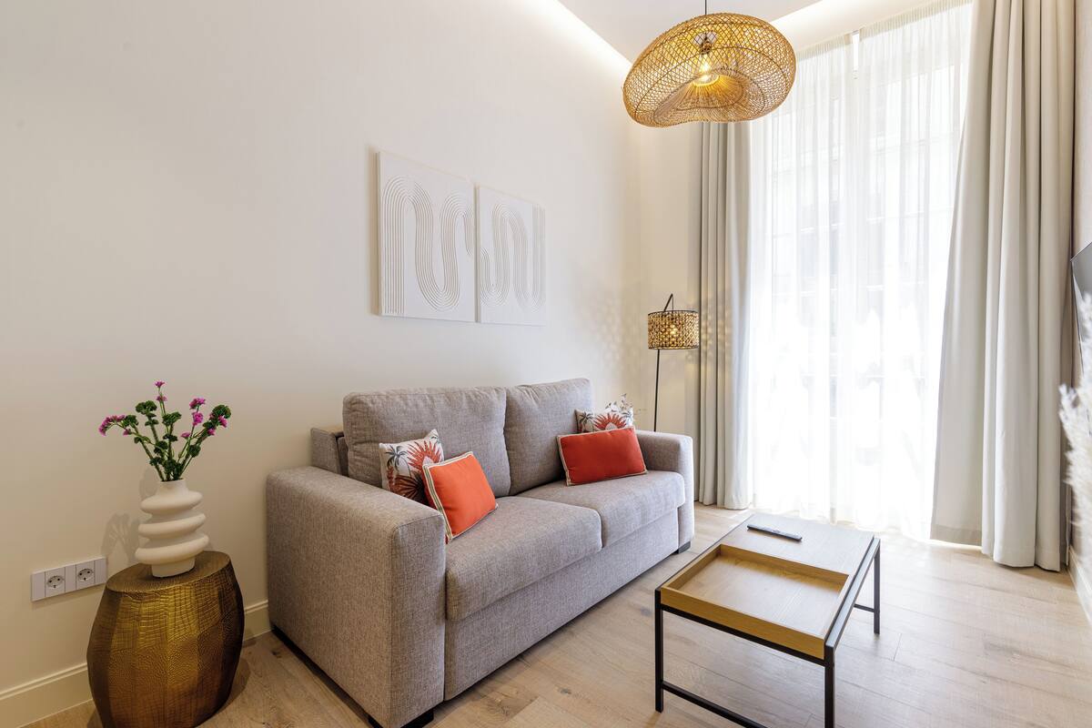 Una sala de estar moderna con un sofá gris, una mesita de centro de madera, un jarrón con flores y una lámpara colgante.