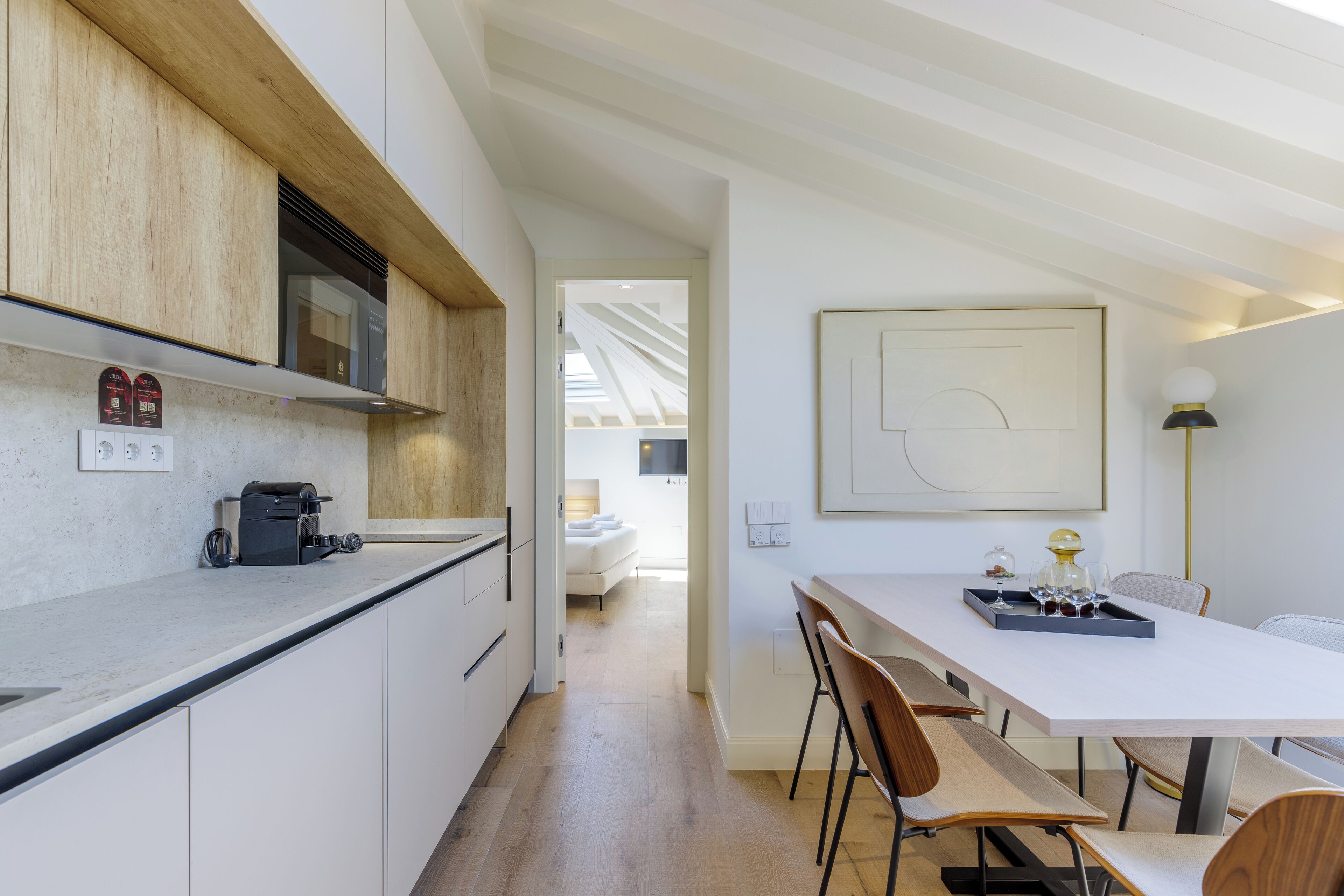A modern kitchen with white cabinets, a countertop with a coffee machine, and a dining area with a white table and chairs.