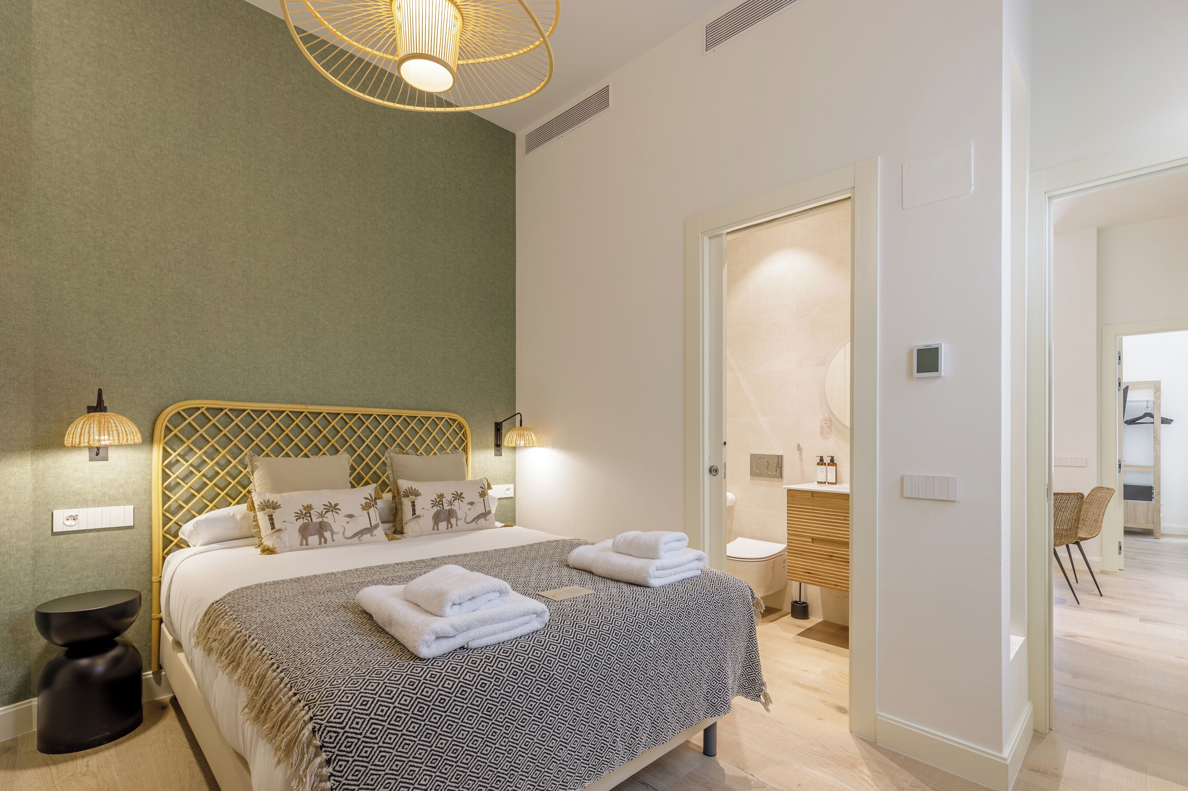 Un dormitorio ordenado con cama, lámparas de noche y un baño visible a través de una puerta abierta.
