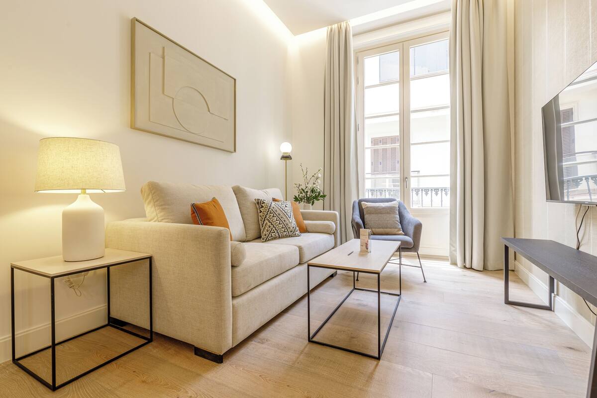Una sala de estar moderna con un sofá, una mesa de centro, una mesita auxiliar con lámpara, una silla y un televisor.