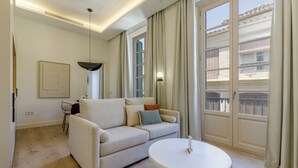 Een moderne woonkamer met een bank, een ronde salontafel, een hanglamp en uitzicht op een gebouw door grote ramen.