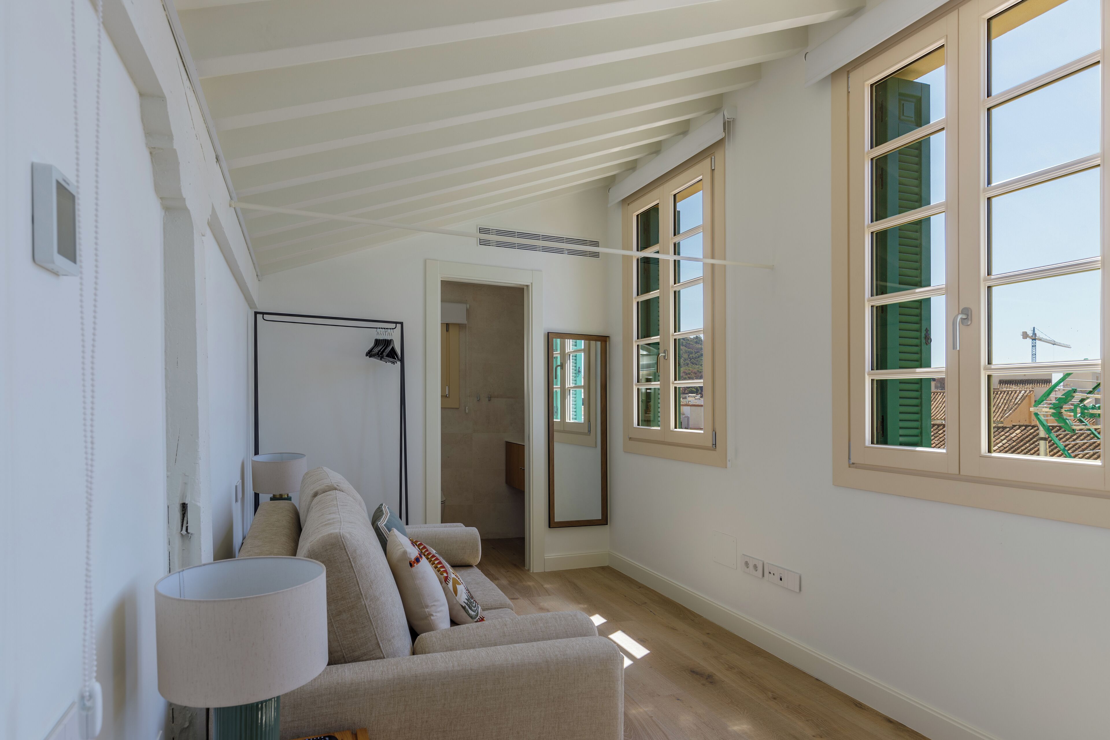 A spacious room with a high ceiling, a large window with shutters, a sofa, and a lamp.