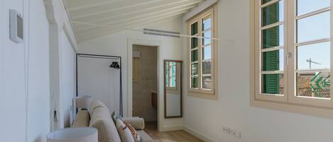 A spacious room with a high ceiling, a large window with shutters, a sofa, and a lamp.