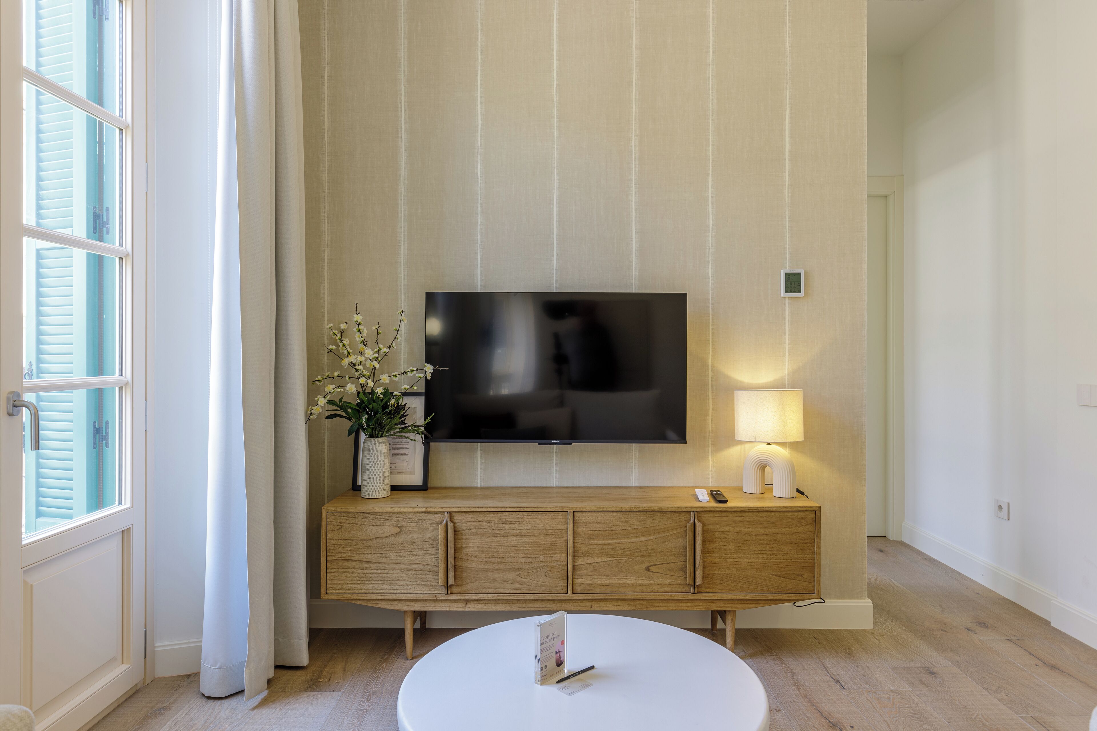 A modern living room with a flat-screen TV mounted on the wall, a wooden console table with a lamp, and a round coffee table.
