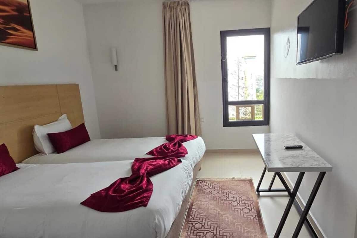 Une chambre d’hôtel avec deux lits, une télévision, une fenêtre et une petite table.