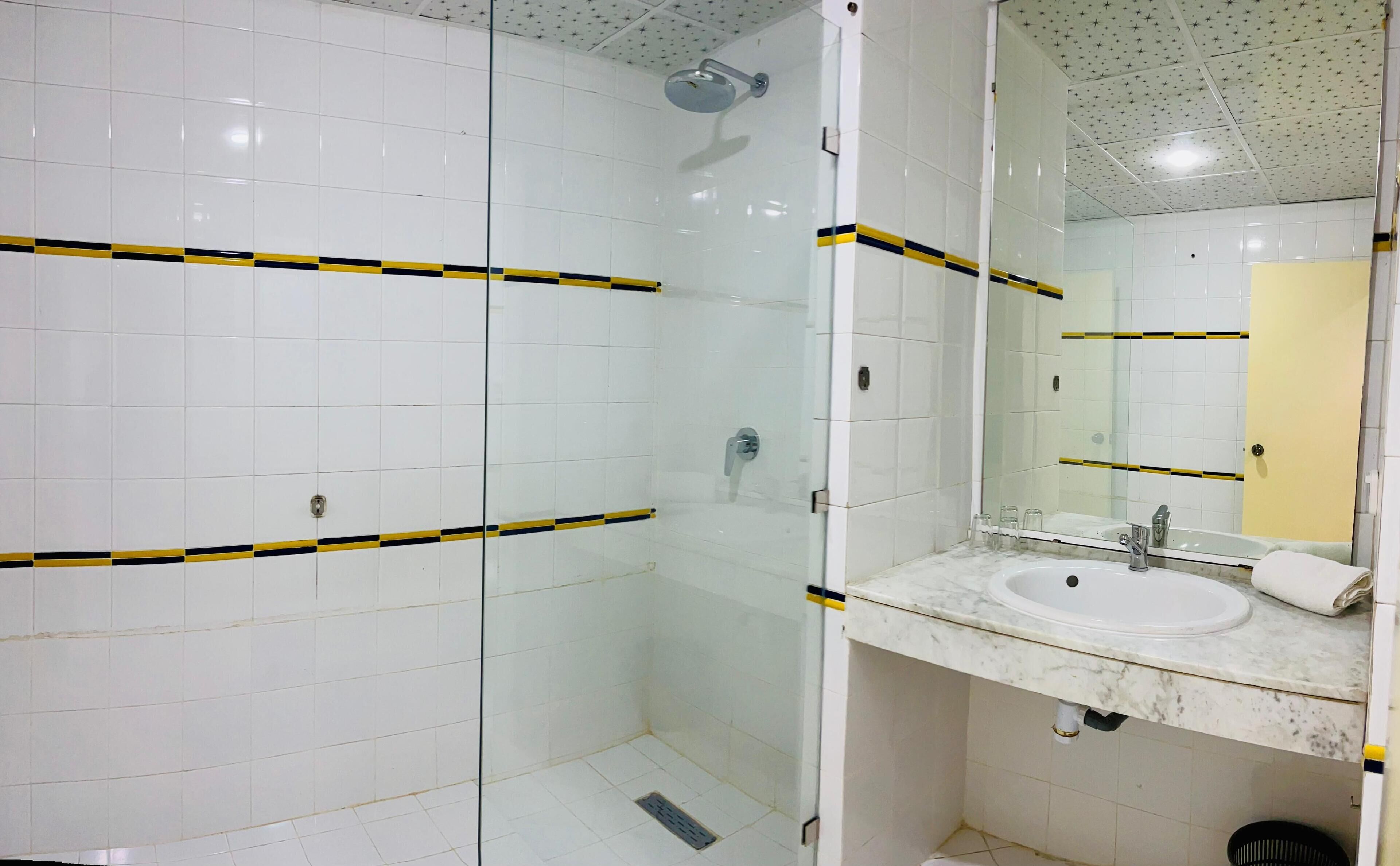 A bathroom with white tiles, a glass shower enclosure, a sink with a mirror, and a yellow stripe design on the walls.
