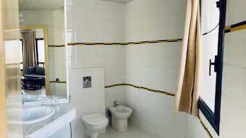 A small, clean bathroom with white tiles, a toilet, a bidet, and a sink.