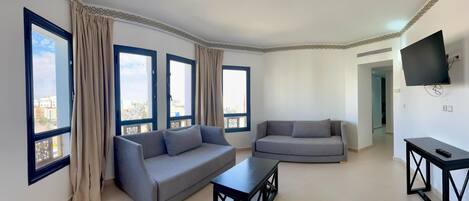 A modern living room with a grey sofa, a smaller grey armchair, a coffee table, and a TV mounted on the wall.