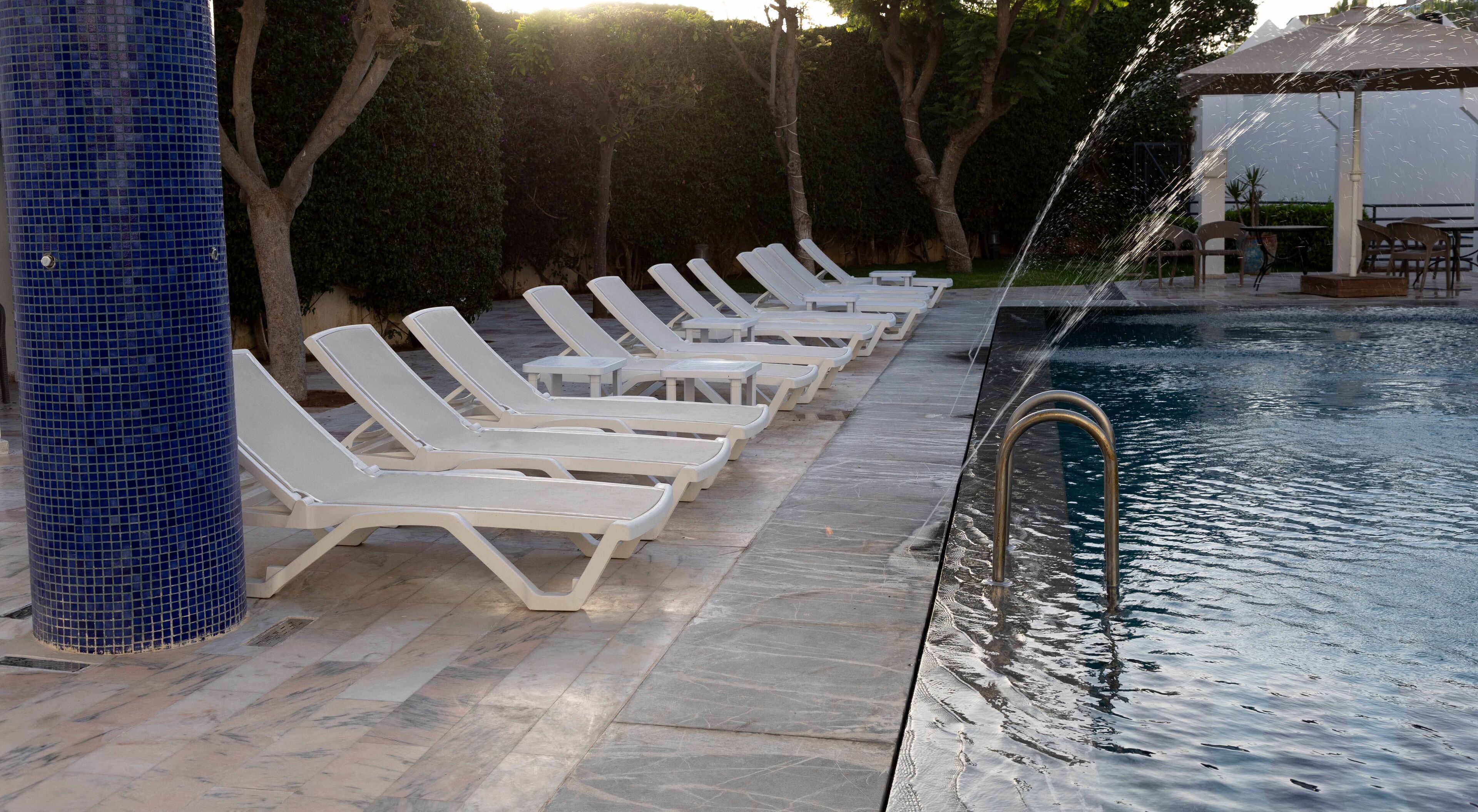 Un espace aménagé au bord de la piscine, avec des chaises longues blanches et une colonne recouverte de carreaux bleus.