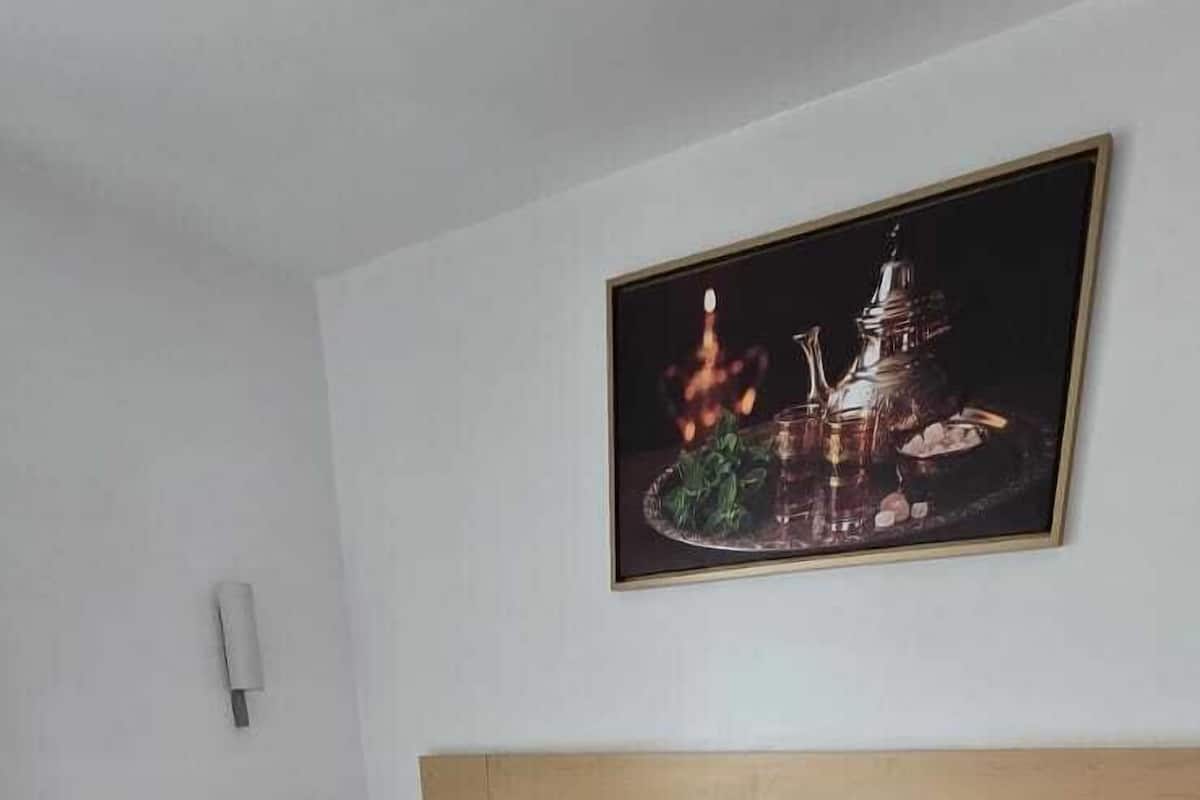 Un lit double avec du linge de lit blanc et des coussins décoratifs rouges, une tête de lit en bois et un tableau encadré au-dessus.