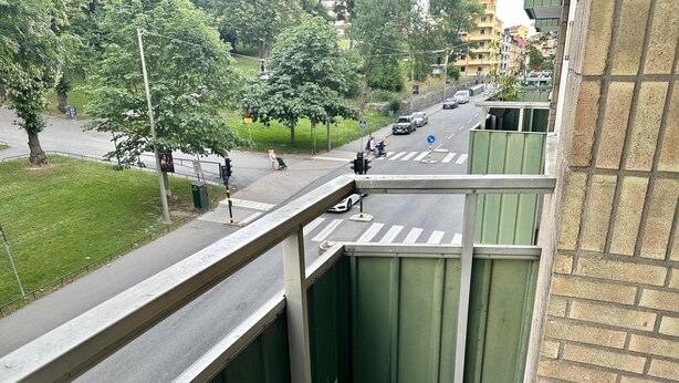 Une vue depuis un balcon donnant sur une rue animée, où l’on peut voir des voitures et des piétons.
