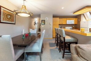 A modern kitchen with wooden cabinets, a microwave, and a refrigerator. There is a dining area with a dark wooden table and matching chairs. - Spacious Townhome Two Minutes from the Lift (Keystone)