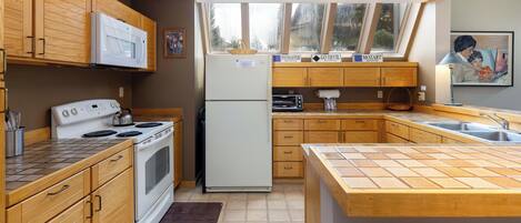 A kitchen with wooden cabinets, a microwave, stove, refrigerator, and a window with a view of trees.