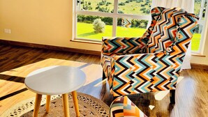 A room with a large window, a patterned armchair, a small round table, and a woven rug. - Lookout sirwa
 (Naivasha)